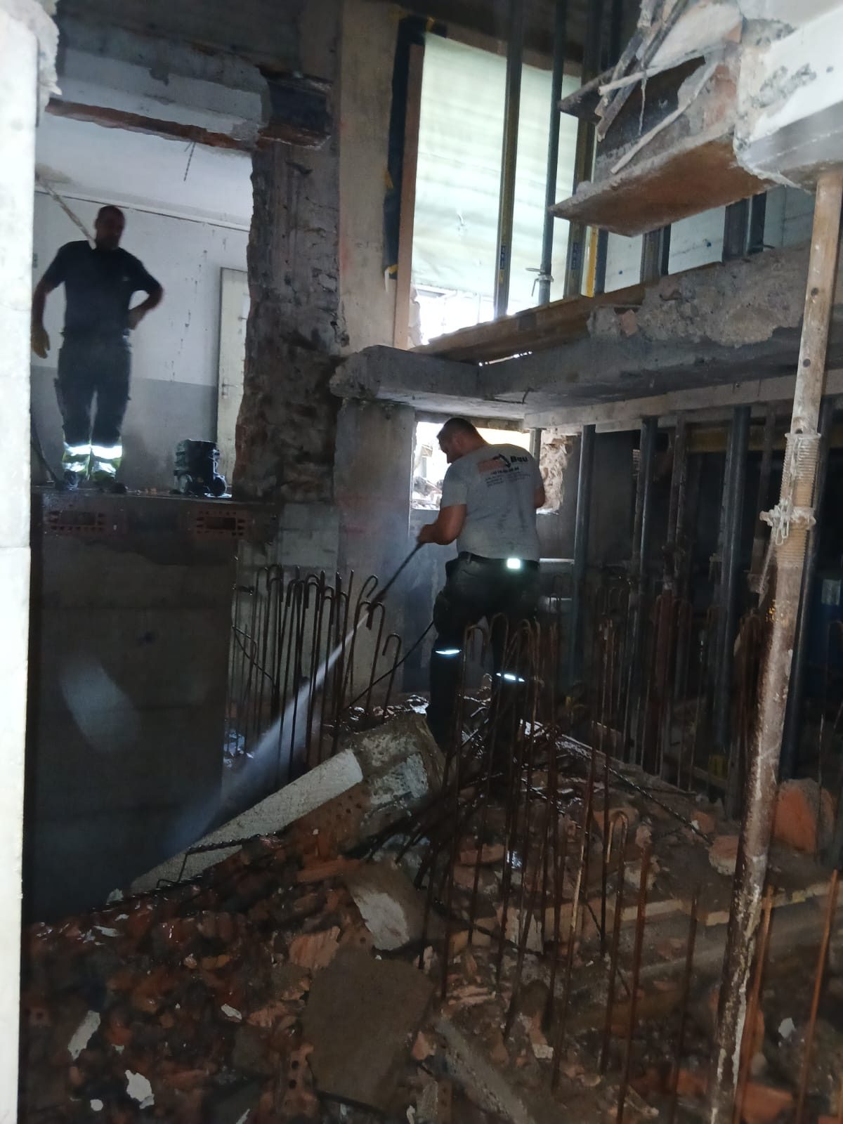 Zwei Arbeiter im entkernten Rohbau, einer spritzt den Schutt ab